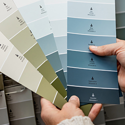 Person holding a fan of blue and green paint color swatches displaying various shades.